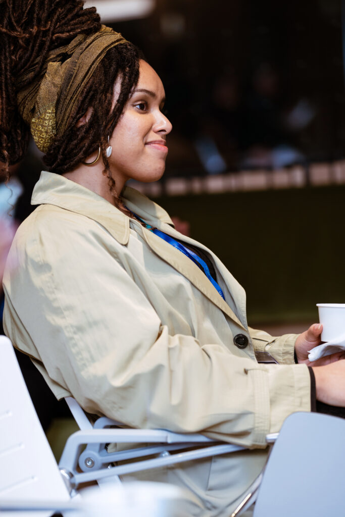 A Black person sits in a chair looking to the front of the room.