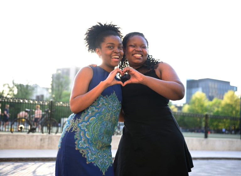 Two Black students posing for a photo, creating a joined heart shape with their hands.