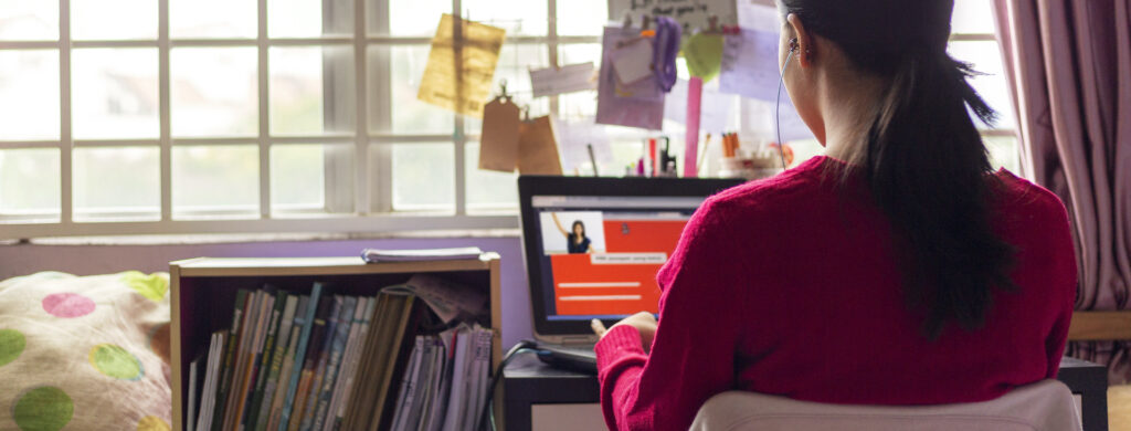 Teenage girl wearing earphones sitting in front of laptop, attending online video class