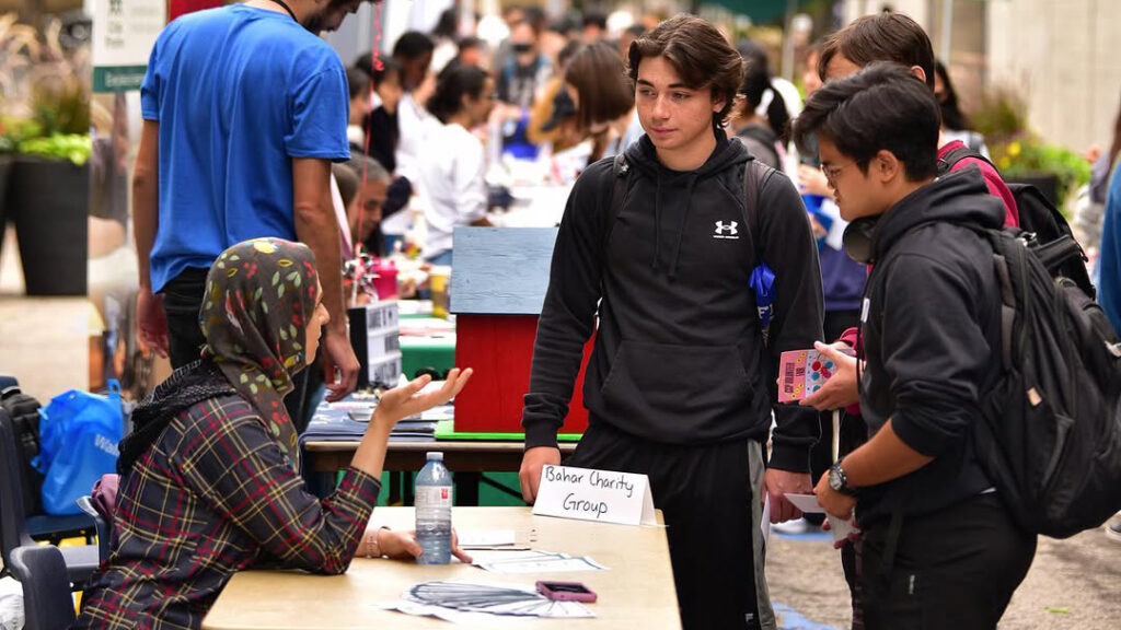 Two people stand and speak to a person seated at a volunteer fair table.