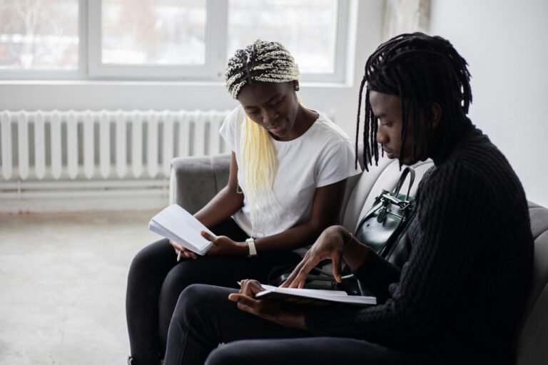 Two black students sitting on a couch looking at a book together