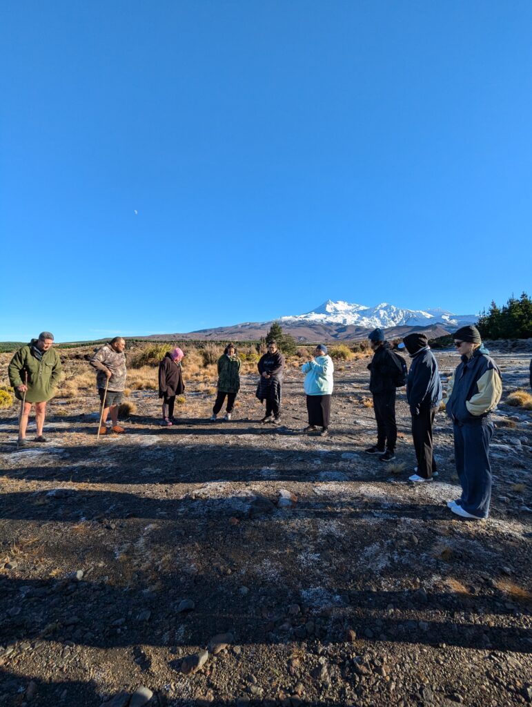 Group of students standing in a large semi circle outside against the New Zealand skyline with a mountain in the background